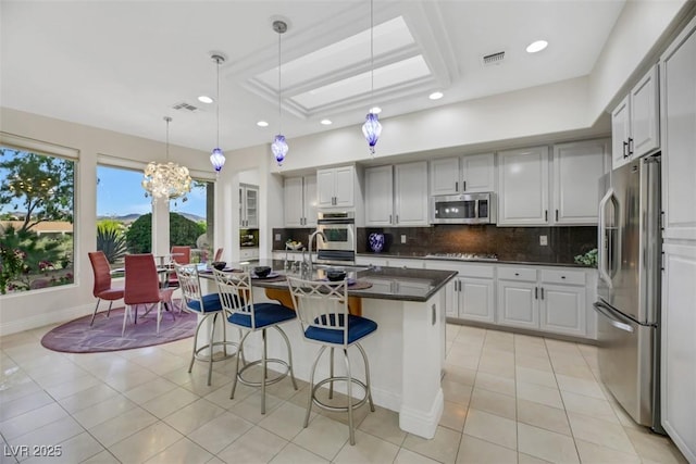 kitchen with appliances with stainless steel finishes, a kitchen breakfast bar, decorative backsplash, hanging light fixtures, and a kitchen island with sink