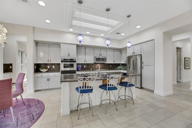 kitchen featuring appliances with stainless steel finishes, tasteful backsplash, a kitchen breakfast bar, hanging light fixtures, and a raised ceiling