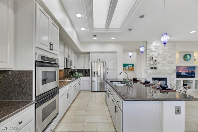 kitchen with sink, appliances with stainless steel finishes, an island with sink, pendant lighting, and white cabinets