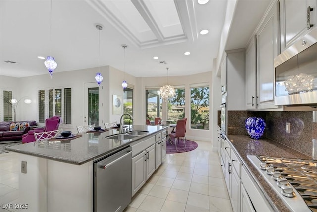 kitchen featuring sink, hanging light fixtures, appliances with stainless steel finishes, a kitchen island with sink, and decorative backsplash