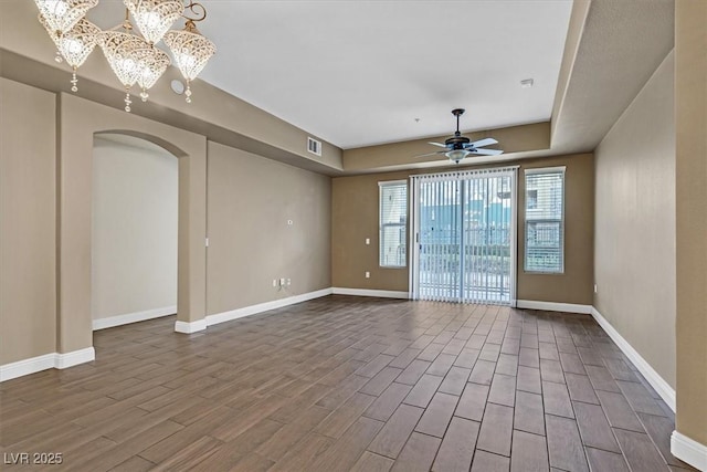 empty room with baseboards, visible vents, arched walkways, wood finished floors, and ceiling fan with notable chandelier