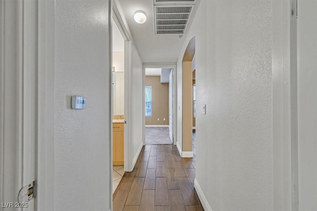 corridor with baseboards, visible vents, wood finished floors, and a textured wall