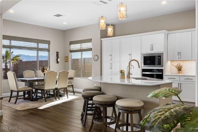 kitchen featuring white cabinetry, black microwave, oven, pendant lighting, and an island with sink