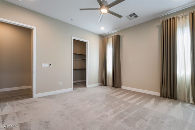 unfurnished bedroom featuring ceiling fan, light colored carpet, a closet, and a walk in closet