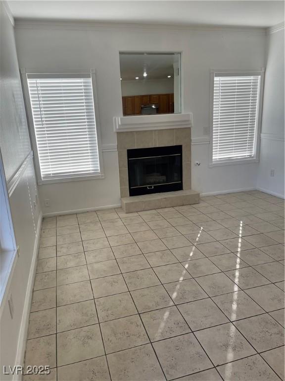 unfurnished living room with a tile fireplace, light tile patterned flooring, and ornamental molding