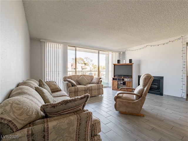 living area with a textured ceiling, a textured wall, a fireplace, wood finished floors, and expansive windows