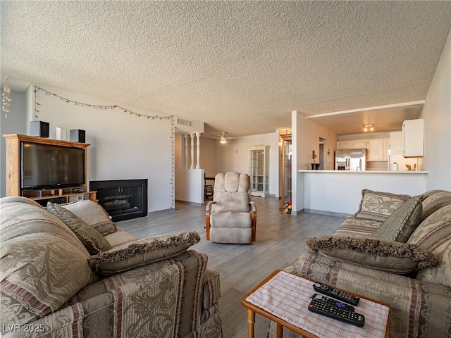 living room with a textured ceiling, a fireplace, wood finished floors, and visible vents