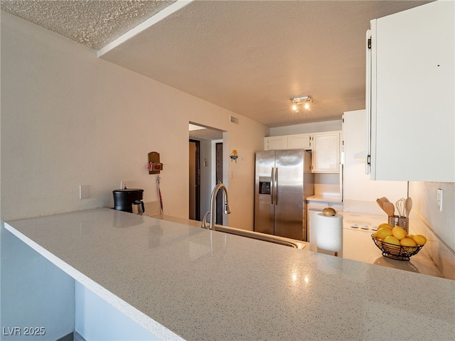 kitchen featuring a sink, a peninsula, stainless steel fridge with ice dispenser, and a textured ceiling