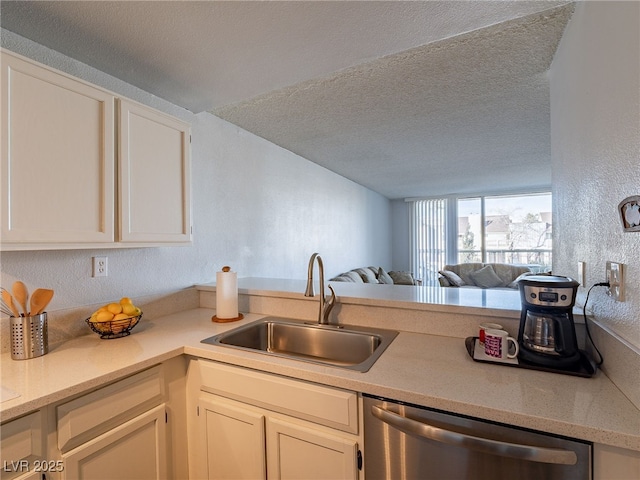 kitchen with open floor plan, light countertops, a textured ceiling, stainless steel dishwasher, and a sink