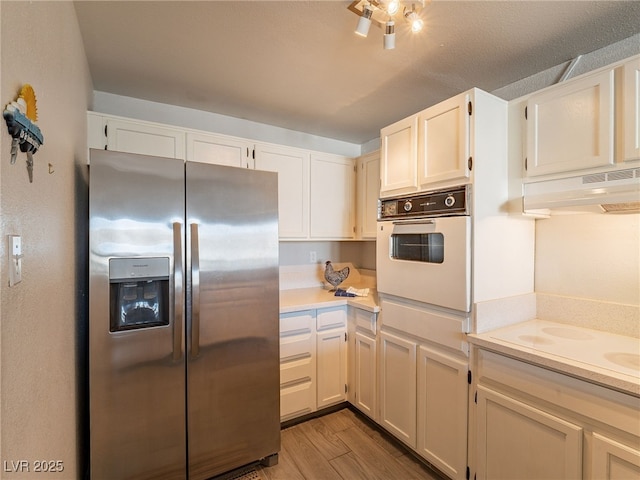 kitchen with white appliances, white cabinets, wood finished floors, light countertops, and under cabinet range hood