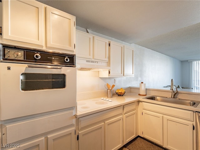 kitchen featuring light countertops, a sink, a textured ceiling, white appliances, and under cabinet range hood