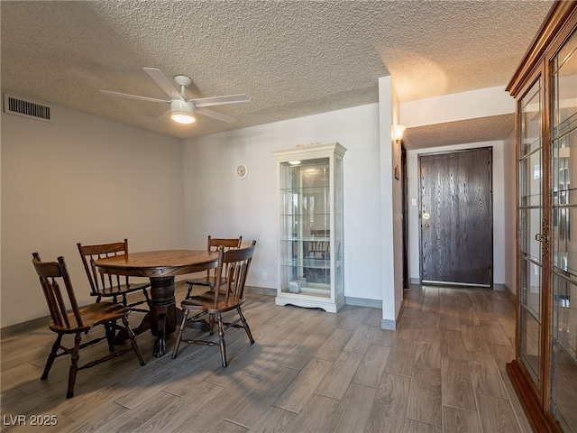 dining space with ceiling fan, a textured ceiling, wood finish floors, visible vents, and baseboards