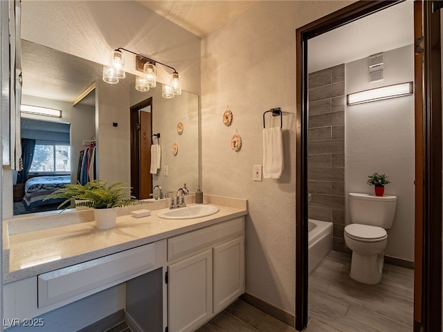 bathroom featuring a textured wall, toilet, wood finished floors, vanity, and baseboards