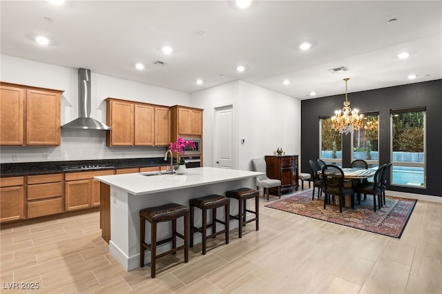 kitchen featuring wall chimney exhaust hood, a breakfast bar, decorative light fixtures, a center island with sink, and stainless steel appliances