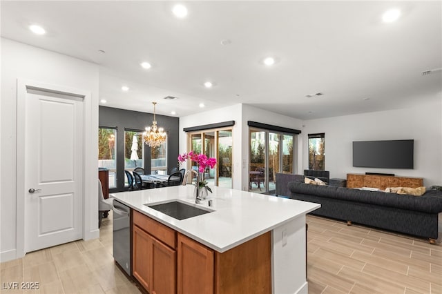 kitchen with pendant lighting, sink, dishwasher, a kitchen island with sink, and a notable chandelier