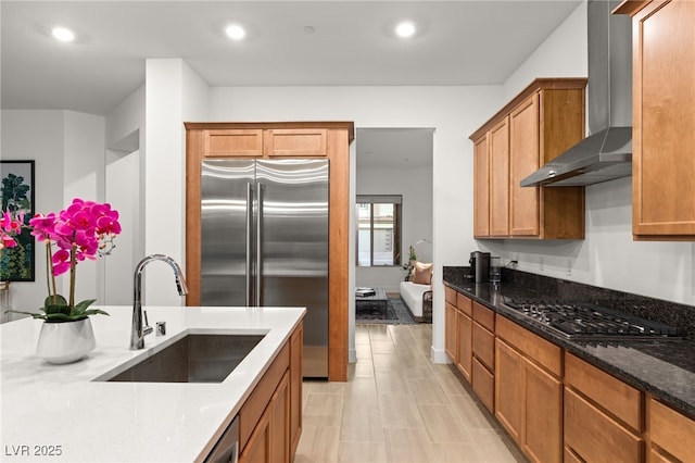 kitchen featuring appliances with stainless steel finishes, stone countertops, sink, and wall chimney exhaust hood