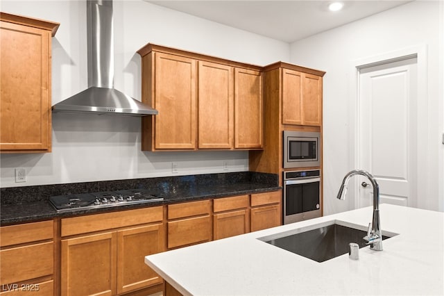 kitchen featuring wall chimney range hood, sink, dark stone counters, and appliances with stainless steel finishes