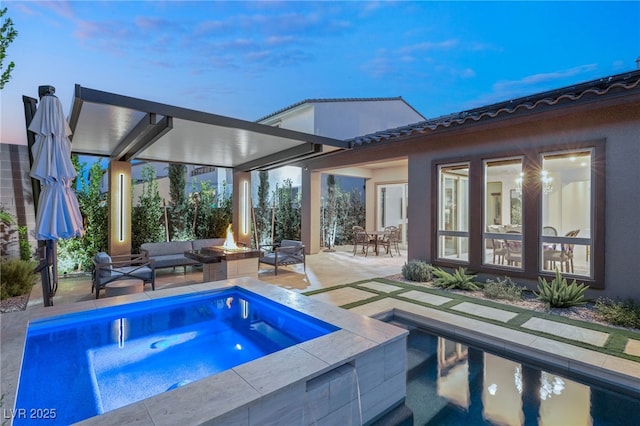 pool at dusk featuring an in ground hot tub, an outdoor living space with a fire pit, and a patio area