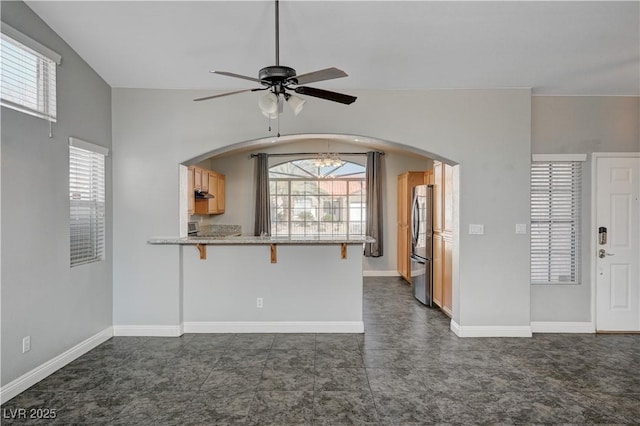 kitchen featuring a breakfast bar area, vaulted ceiling, stainless steel refrigerator, kitchen peninsula, and ceiling fan