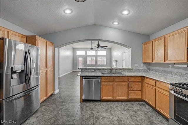 kitchen with vaulted ceiling, appliances with stainless steel finishes, sink, light stone counters, and kitchen peninsula