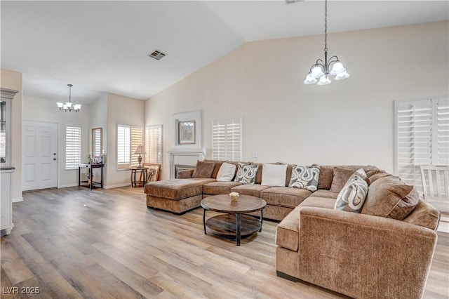 living room featuring light hardwood / wood-style flooring, high vaulted ceiling, and an inviting chandelier