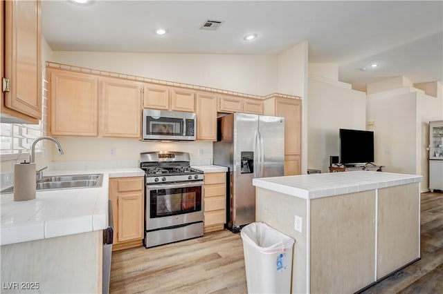 kitchen with light brown cabinetry, light wood-type flooring, stainless steel appliances, sink, and lofted ceiling