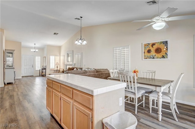 kitchen featuring dark hardwood / wood-style flooring, ceiling fan with notable chandelier, tile countertops, decorative light fixtures, and a center island