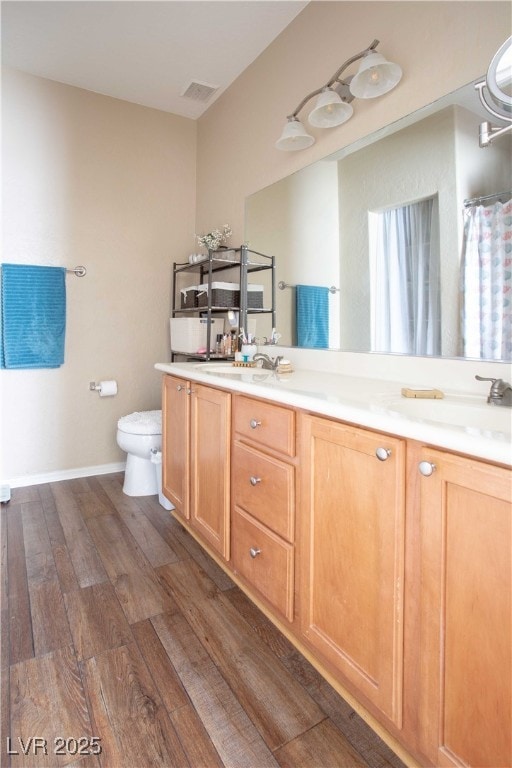 bathroom with visible vents, baseboards, toilet, double vanity, and wood finished floors