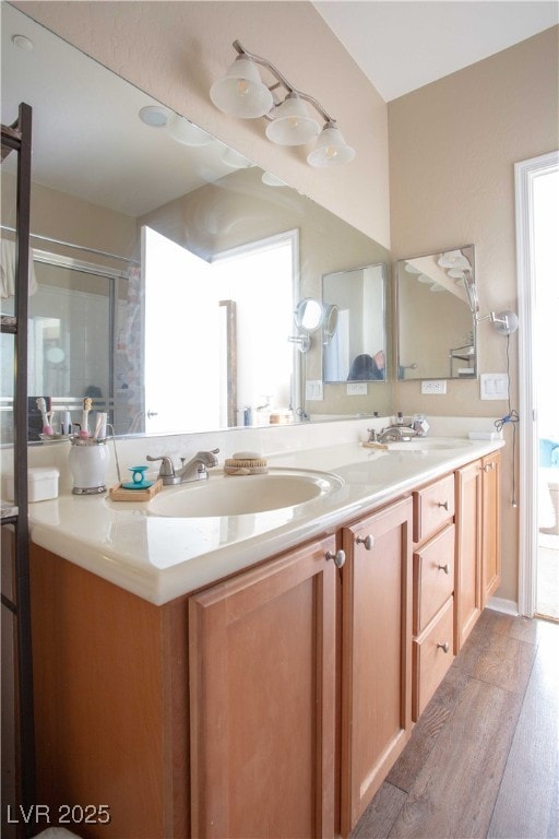 full bath featuring a sink, a shower with door, wood finished floors, and double vanity