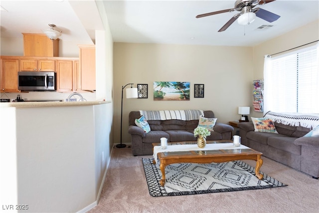 living room featuring visible vents, light colored carpet, baseboards, and a ceiling fan