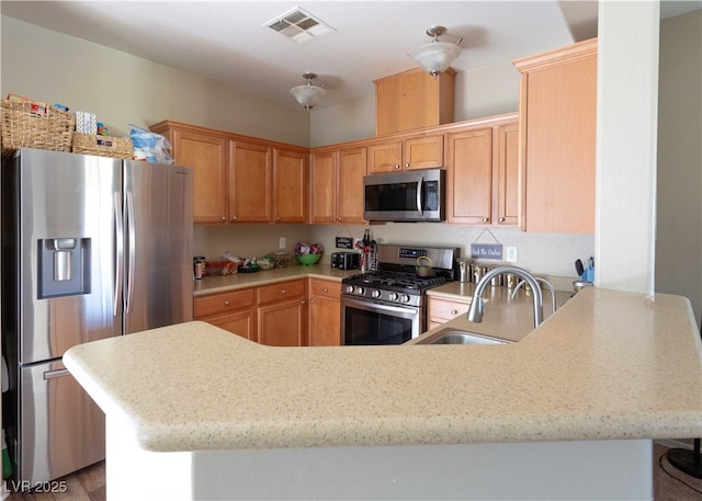 kitchen featuring visible vents, a sink, appliances with stainless steel finishes, a peninsula, and light stone countertops