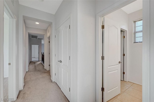 hallway featuring light tile patterned flooring, visible vents, and light colored carpet