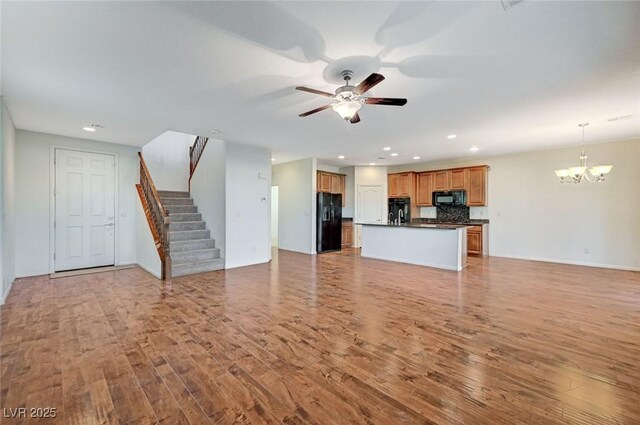 unfurnished living room with ceiling fan with notable chandelier and light hardwood / wood-style floors