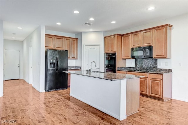 kitchen with a sink, visible vents, light wood-style floors, black appliances, and dark stone countertops