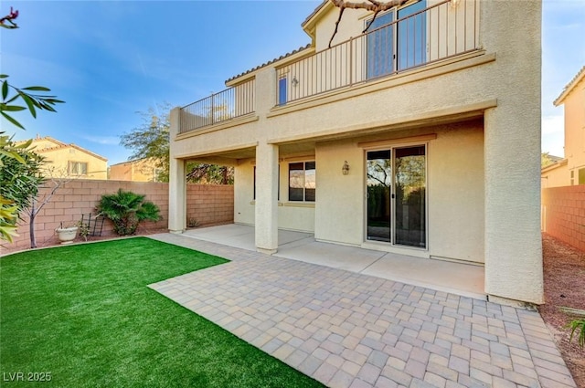 rear view of property with a lawn, a balcony, a fenced backyard, a patio area, and stucco siding