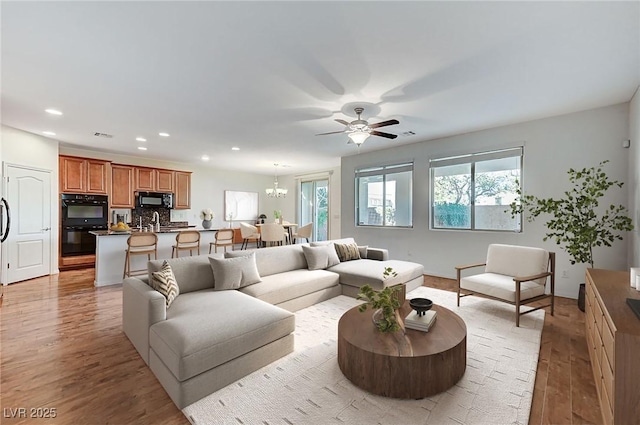 living area featuring recessed lighting, light wood finished floors, and ceiling fan with notable chandelier