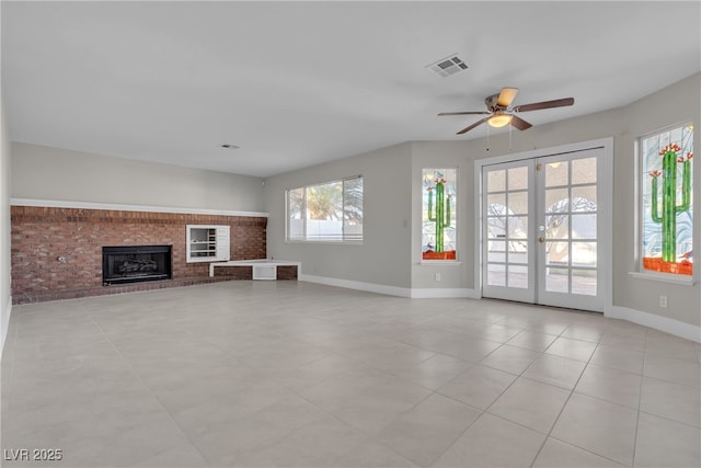 unfurnished living room with a brick fireplace, light tile patterned floors, ceiling fan, and french doors