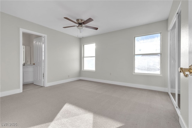 unfurnished bedroom with ceiling fan, light colored carpet, multiple windows, and ensuite bathroom