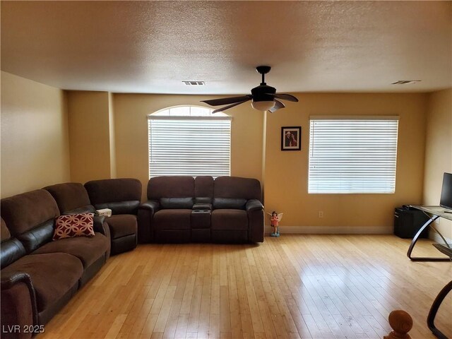 living room with ceiling fan, plenty of natural light, a textured ceiling, and light wood-type flooring