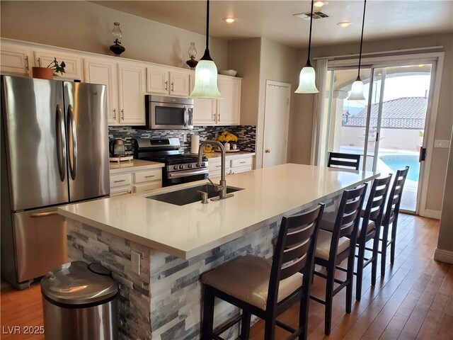 kitchen with stainless steel appliances, decorative light fixtures, an island with sink, and white cabinets