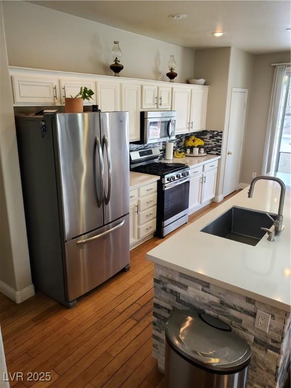 kitchen with sink, appliances with stainless steel finishes, tasteful backsplash, white cabinets, and light wood-type flooring