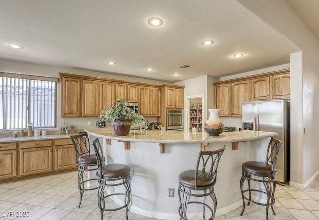 kitchen with a center island, stainless steel appliances, a kitchen breakfast bar, light stone counters, and light tile patterned floors