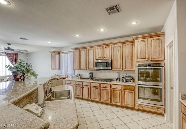 kitchen with ceiling fan, sink, light tile patterned floors, light stone countertops, and stainless steel appliances