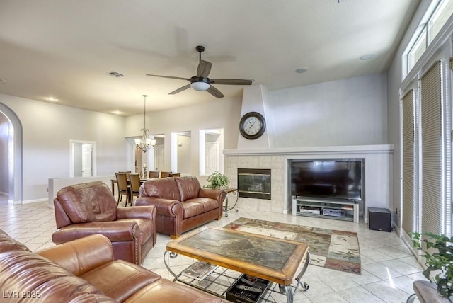 living room featuring a tiled fireplace, ceiling fan with notable chandelier, and light tile patterned floors