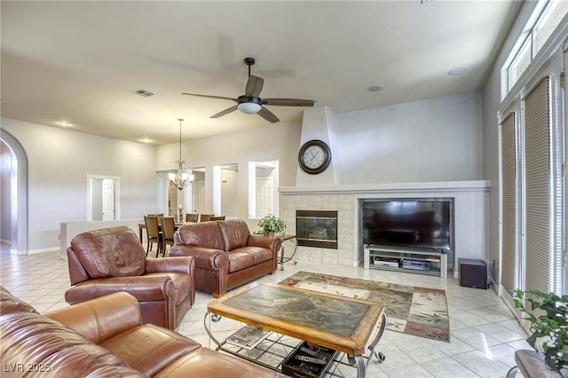 living room featuring ceiling fan with notable chandelier, light tile patterned floors, and a tile fireplace