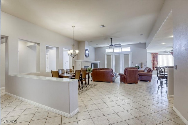 interior space with a tile fireplace, ceiling fan with notable chandelier, pendant lighting, and light tile patterned floors