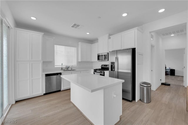 kitchen with appliances with stainless steel finishes, sink, a center island, light hardwood / wood-style floors, and white cabinetry