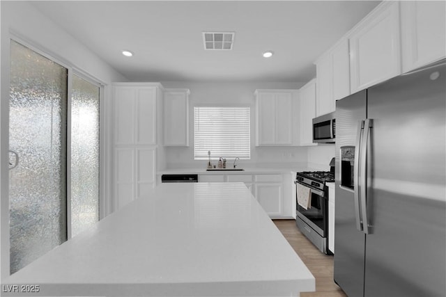 kitchen with white cabinetry, sink, light hardwood / wood-style flooring, a kitchen island, and appliances with stainless steel finishes