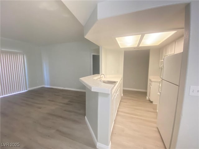 interior space with kitchen peninsula, white cabinetry, sink, and white fridge