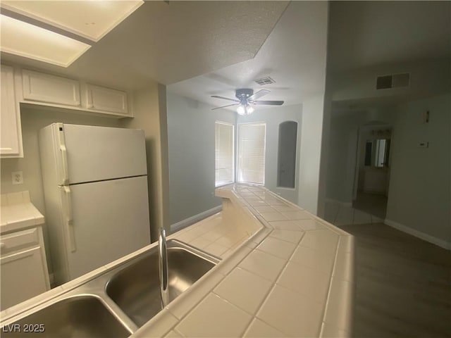 kitchen featuring white refrigerator, sink, ceiling fan, tile counters, and white cabinetry